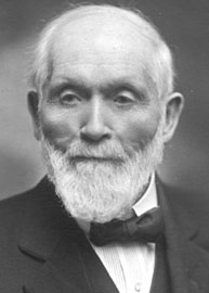 Portrait of James Wallace Collins.  An older gentleman with receding white hair, white beard and mustache.  He is dressed in a dark suit, white shirt, and a trim dark bow tie.